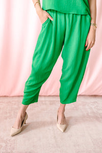 Close-up of bright green harem-style crop pants with elasticized waist and side pockets, paired with nude pointed-toe heels