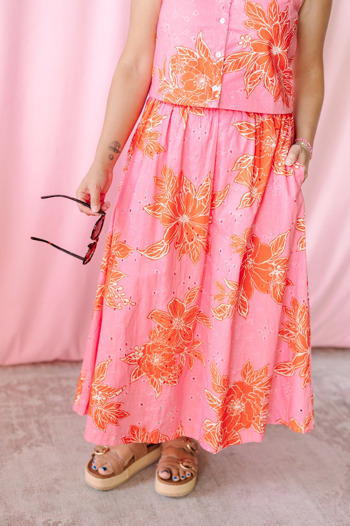 Close-up of pink and orange floral eyelet A-line maxi skirt with elasticized waist and side pocket, paired with platform sandals