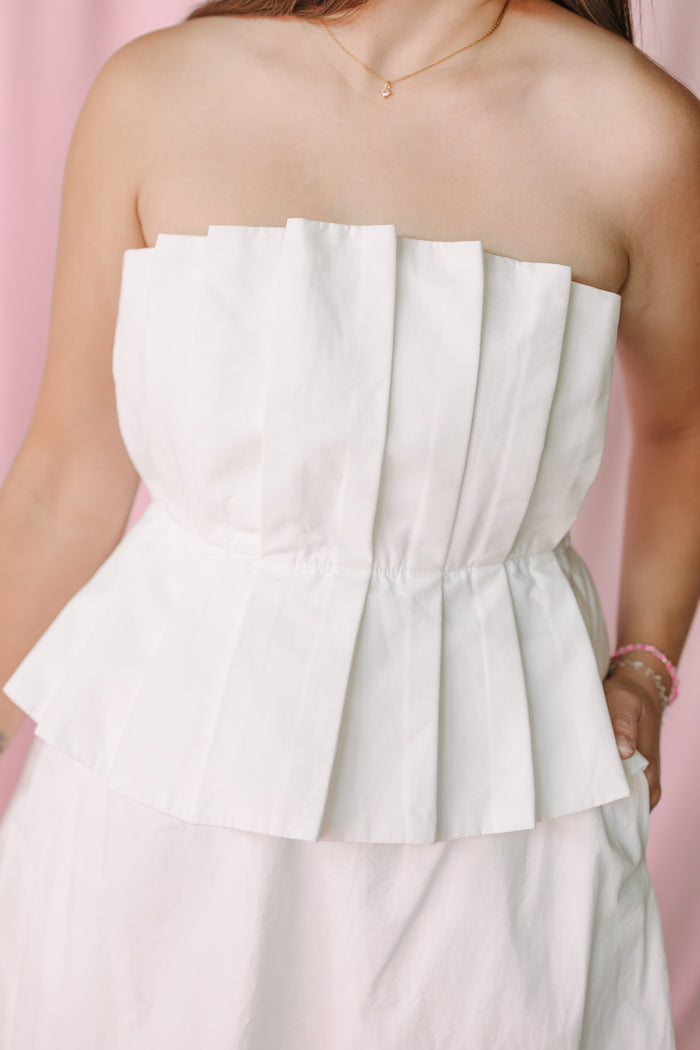 Close-up of white strapless pleated peplum dress with elasticized waist and A-line skirt