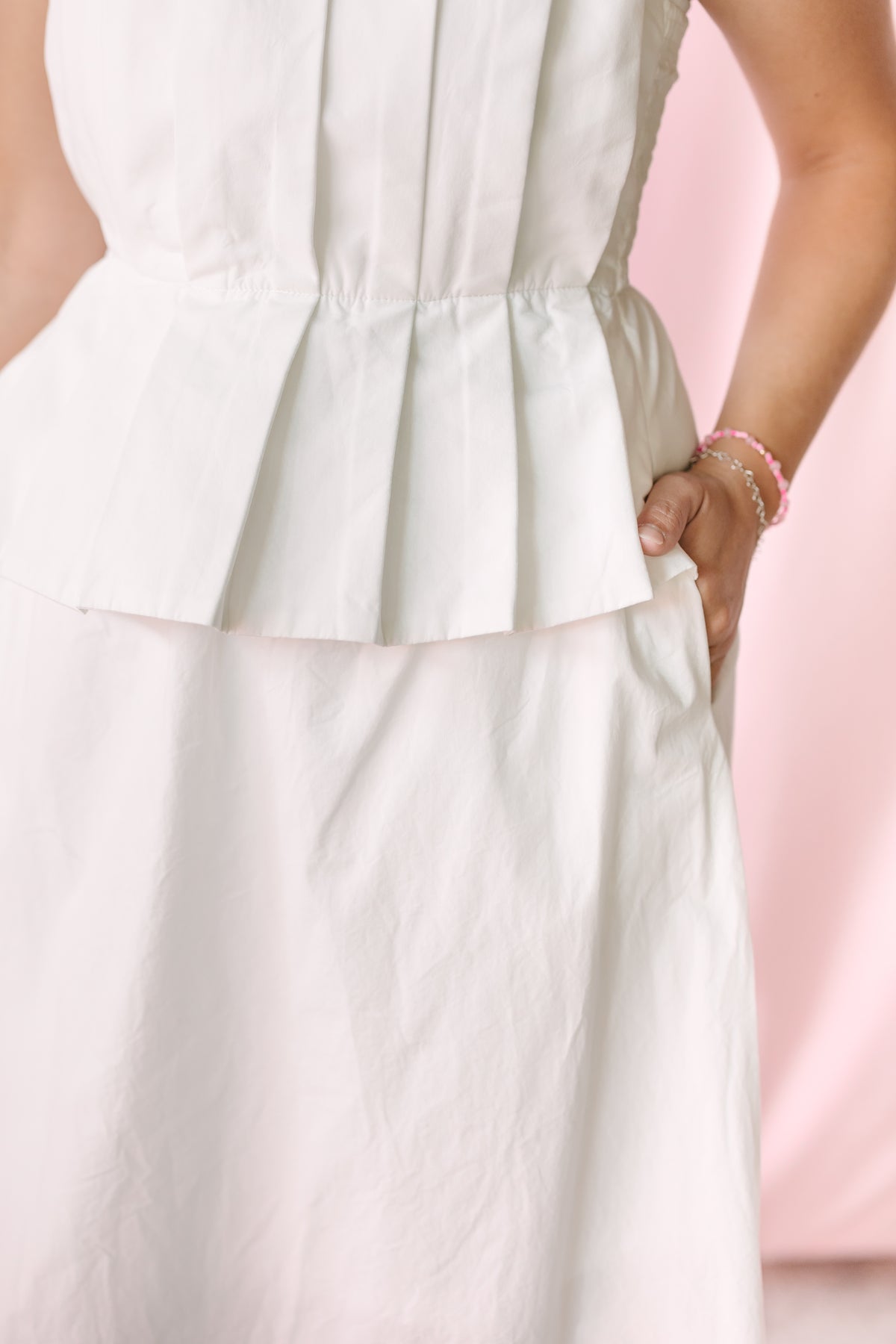 Detail shot of white pleated peplum dress waistline and pocket, showing elasticized waist construction and peplum hem