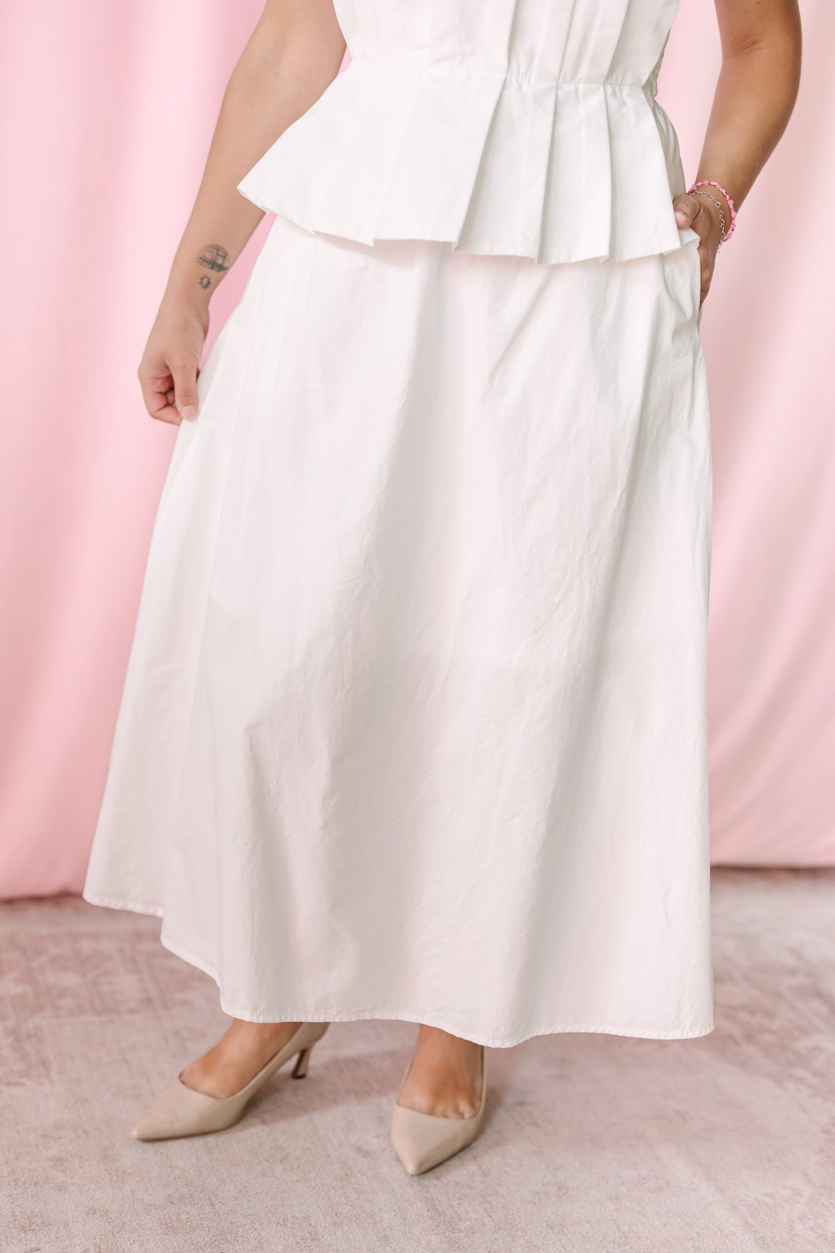 Close-up of white A-line midi skirt portion of strapless peplum dress with side pocket detail and nude heels