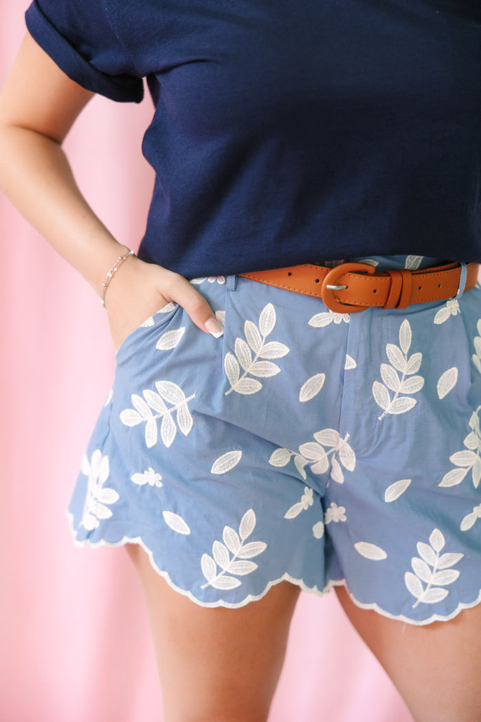 Blue chambray shorts with white embroidered leaf pattern and scalloped hem, styled with a tan leather belt