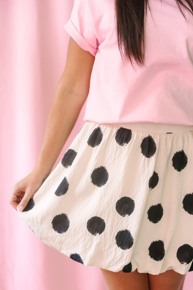 Close-up of a cream bubble skirt with large black brushstroke polka dots, featuring an elastic waistband, paired with a light pink short-sleeve cropped tee
