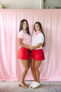 Two women wearing red shorts styled two ways — one with a pink tee and polka dot tie belt, the other with a white tee and red paisley neck scarf