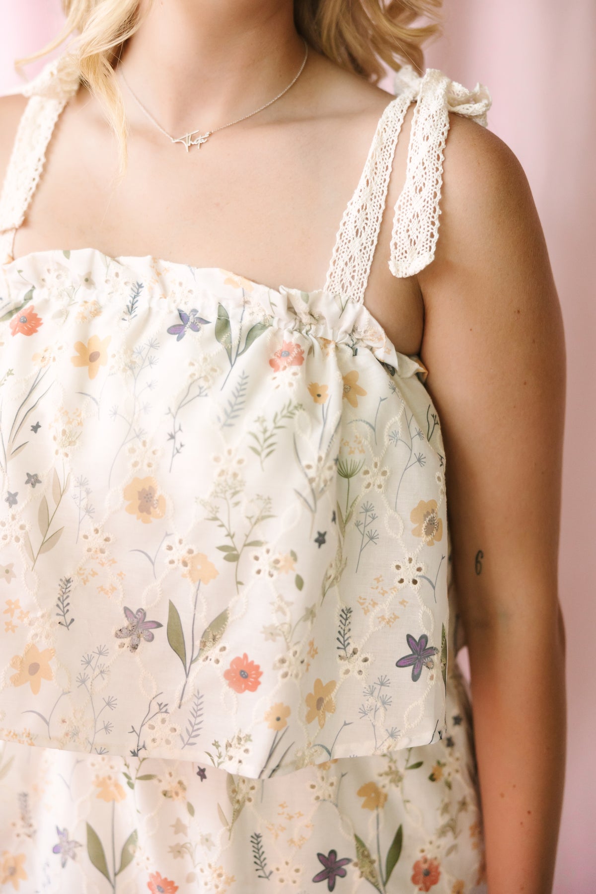 Close-up of the bodice and lace-trimmed tie straps of a cream floral sundress, featuring a gathered square neckline and a delicate wildflower print