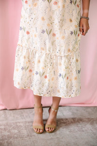 Lower half of a cream floral midi dress with a tiered ruffle hem, featuring a scattered wildflower print in soft peach, coral, blue, and green tones, styled with tan block-heel sandals