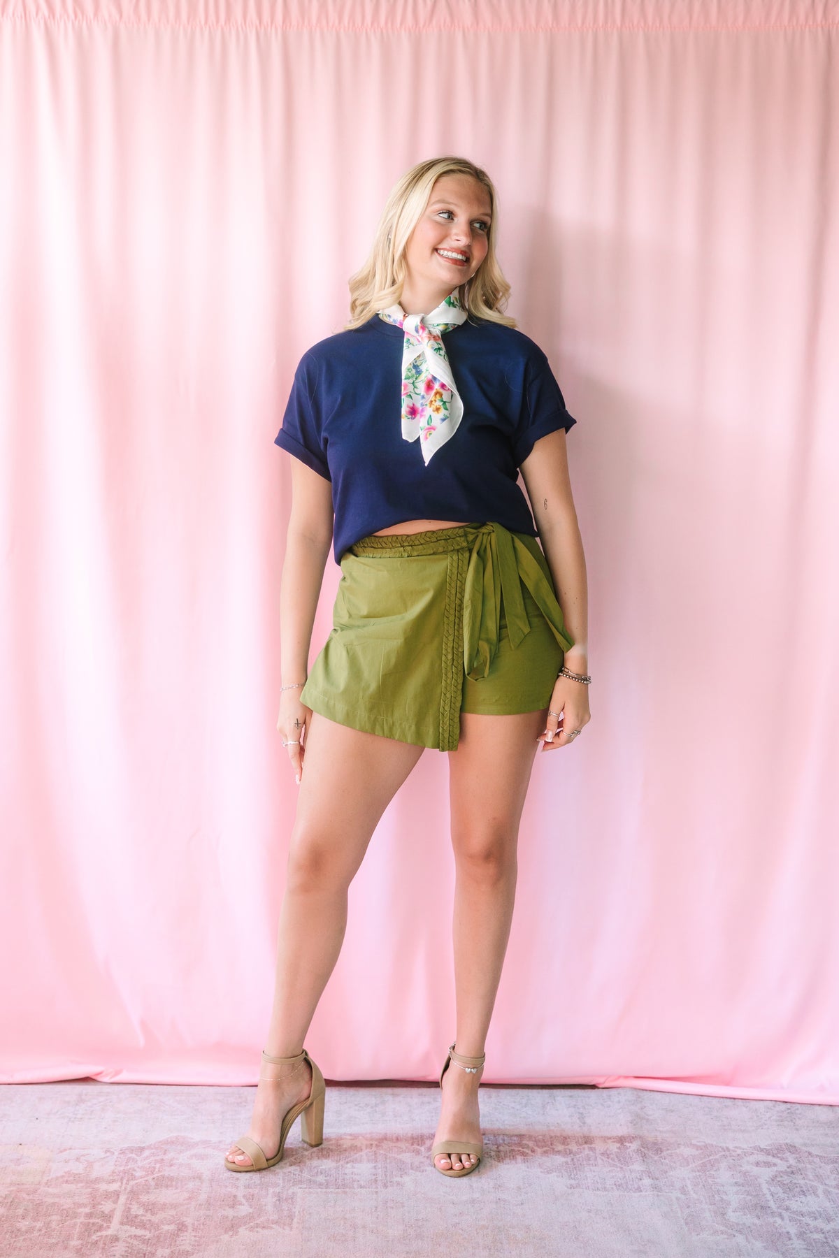 Full-length view of the Green Braided Trim Skort in olive green with wrap-front silhouette, braided trim, and self-tie closure, paired with a navy crop tee, floral scarf, and nude block-heel sandals