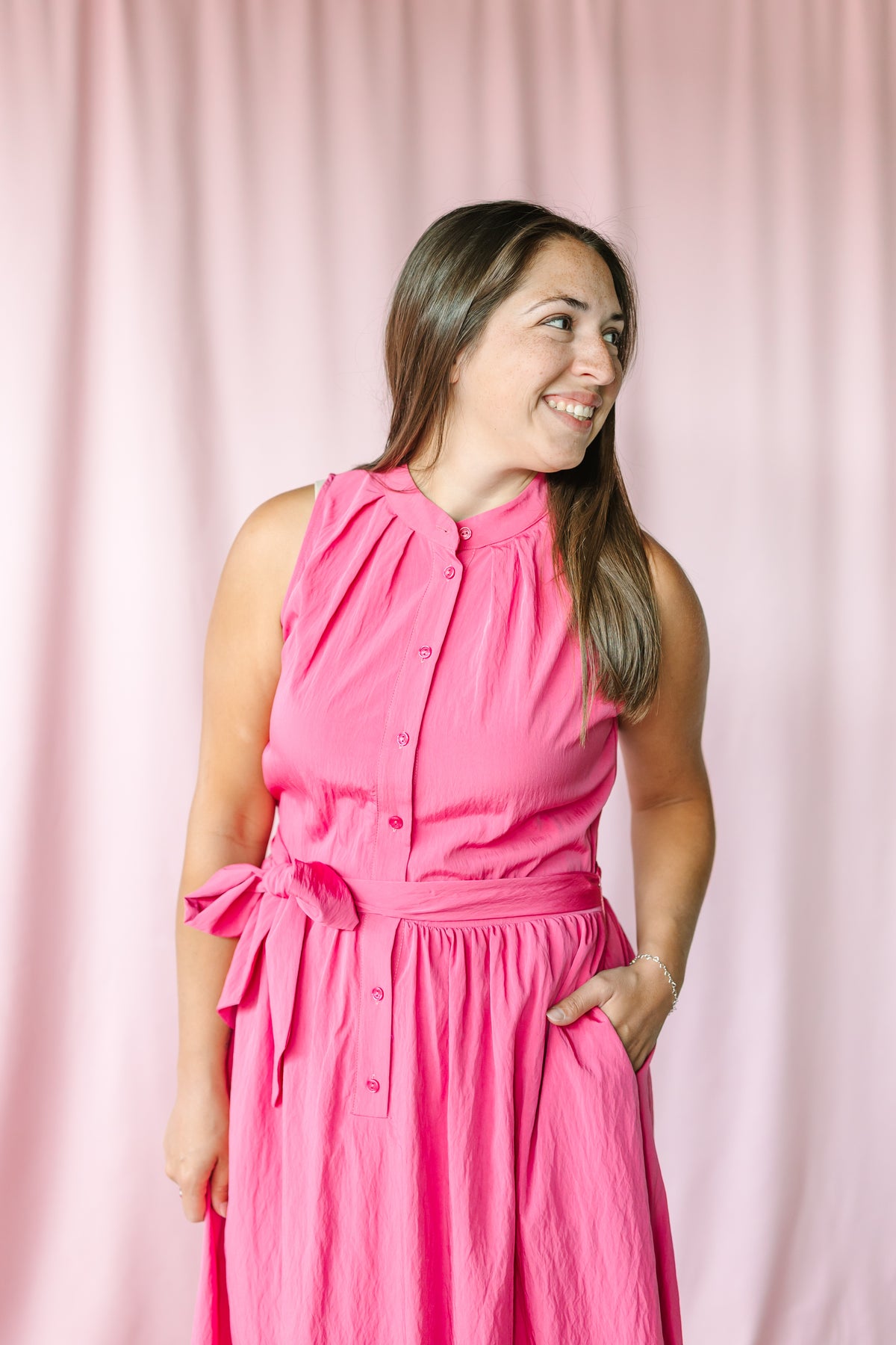 Woman smiling in a berry sleeveless midi dress with button-front bodice, gathered neckline, and side tie belt