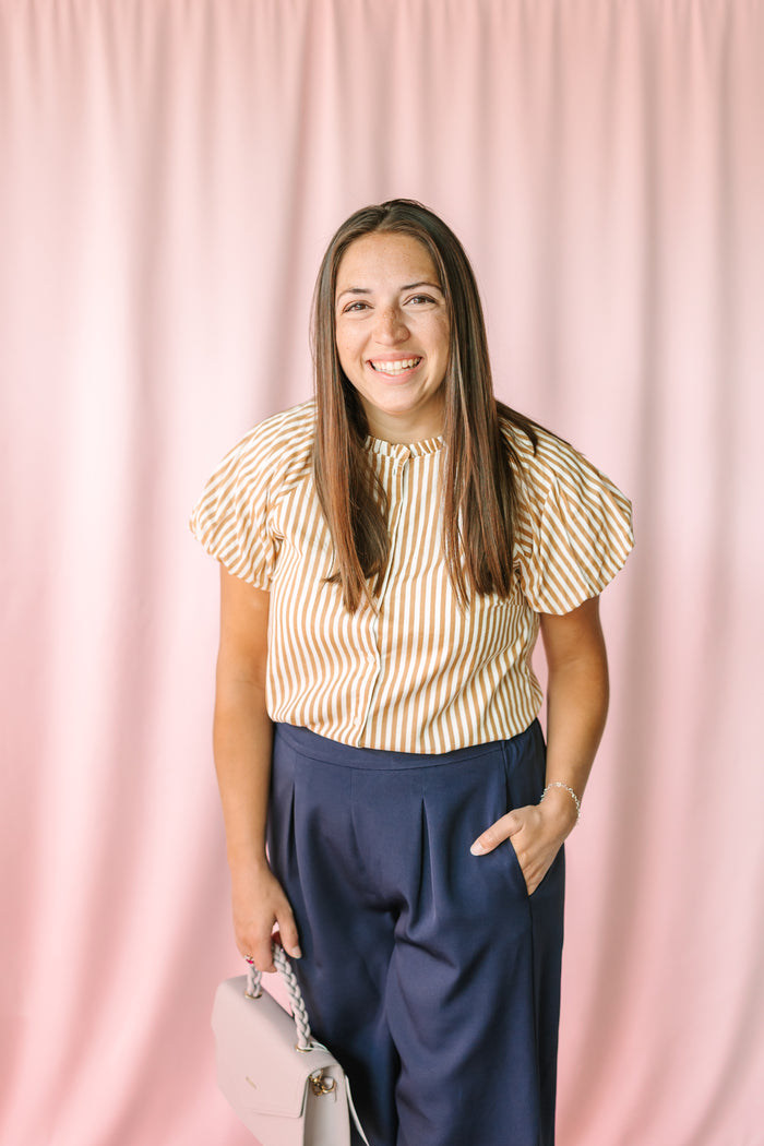 Tan and white striped puff sleeve blouse styled with navy wide-leg trousers and a light purple bag on pink background