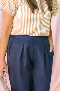 Tan and white striped puff sleeve blouse tucked into navy wide-leg pleated trousers with side pocket detail