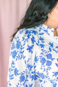 Detail shot of puffed 3/4 sleeve and gathered shoulder on white dress with blue floral print