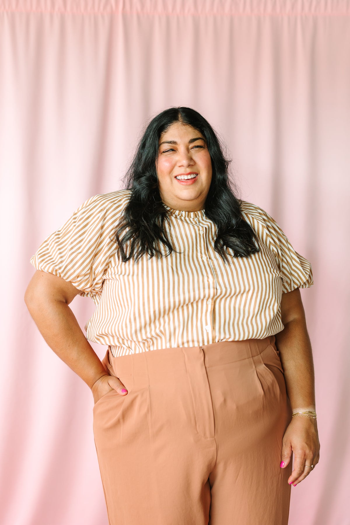 Tan and white striped puff sleeve blouse with ruffle neckline, close-up front view on pink background