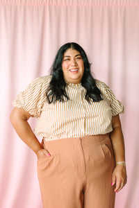 Tan and white striped puff sleeve blouse with ruffle neckline, close-up front view on pink background