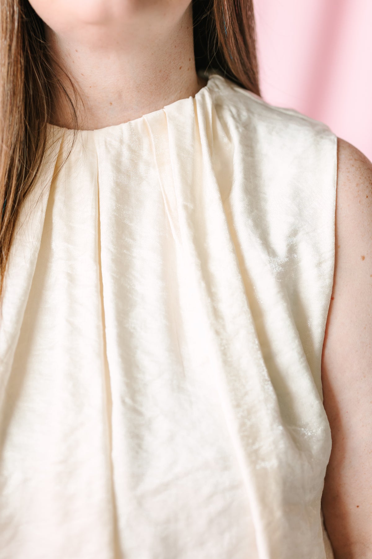 Close-up of mock neckline and pleated bodice detail on cream sleeveless balloon top