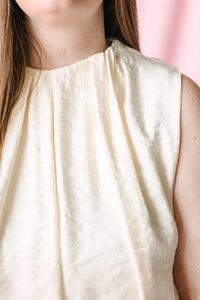 Close-up of mock neckline and pleated bodice detail on cream sleeveless balloon top