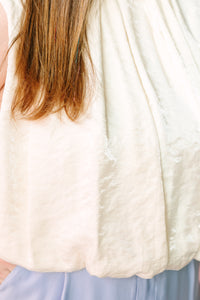 Back and side view of cream sleeveless balloon top showing scalloped hem and pleated texture detail