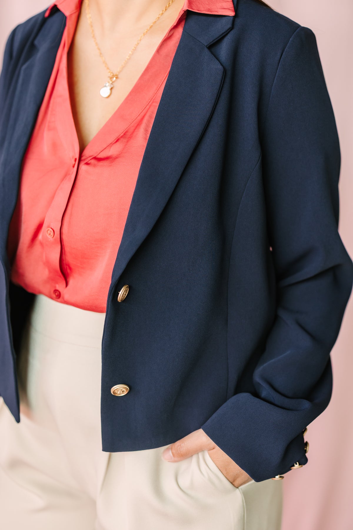 Close-up of navy blazer with gold button detail layered over coral satin button-down blouse with necklace