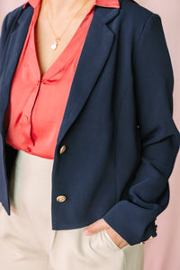 Close-up of navy blazer with gold button detail layered over coral satin button-down blouse with necklace