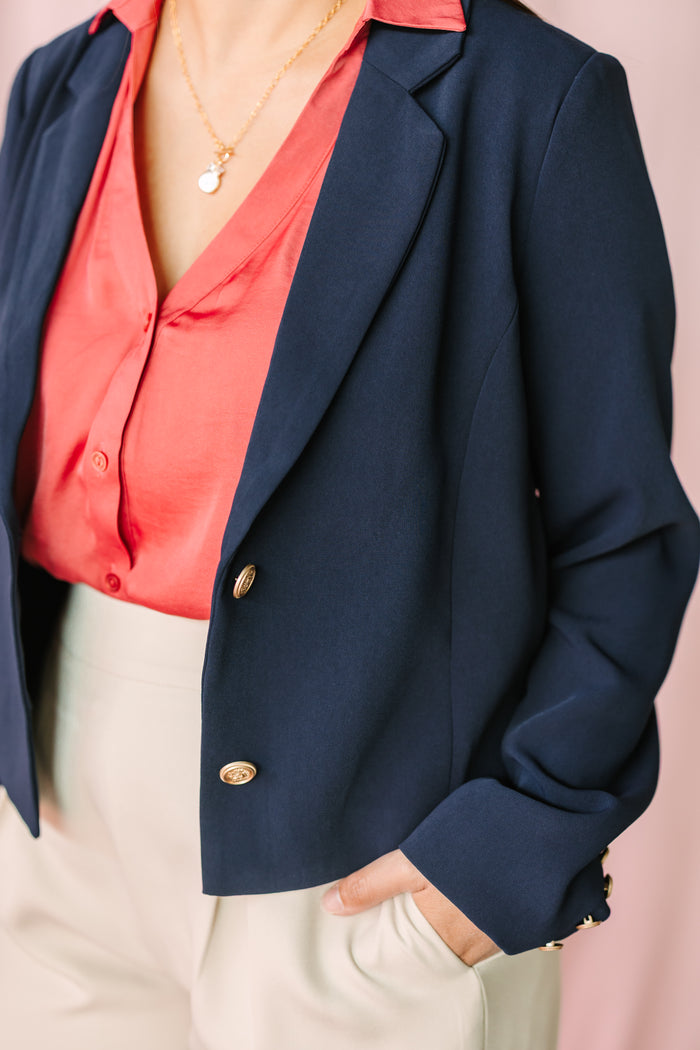 Close-up of navy blazer with gold button detail layered over coral satin button-down blouse with necklace