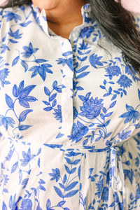 Close-up of white dress bodice featuring intricate blue floral and leaf embroidery-style print with ruffle collar neckline