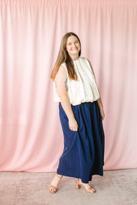 Navy blue gathered maxi skirt with elastic waist shown from side angle, styled with cream sleeveless bubble hem top and nude block heel sandals