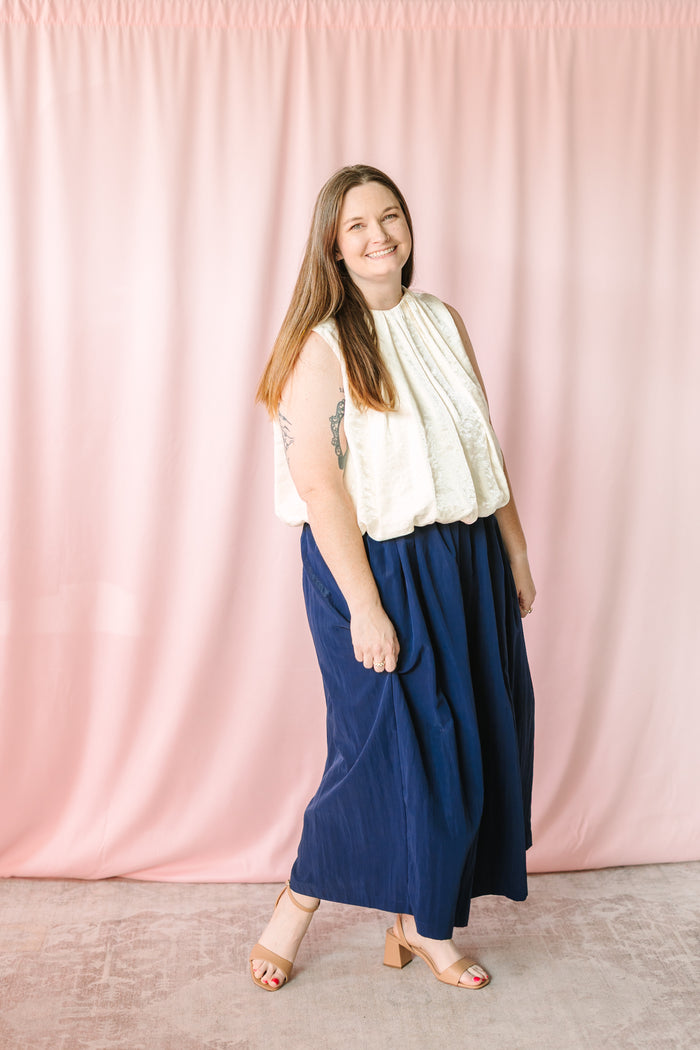 Navy blue gathered maxi skirt with elastic waist shown from side angle, styled with cream sleeveless bubble hem top and nude block heel sandals
