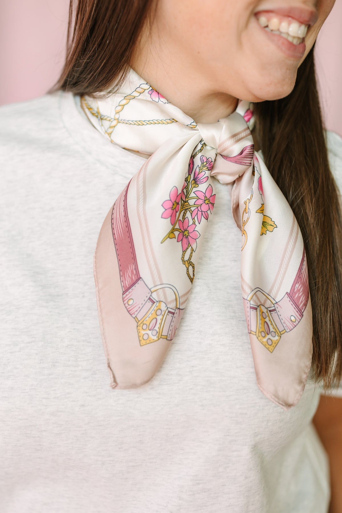Close-up of cream silk scarf with pink floral and belt buckle print tied at neckline over heather gray tee