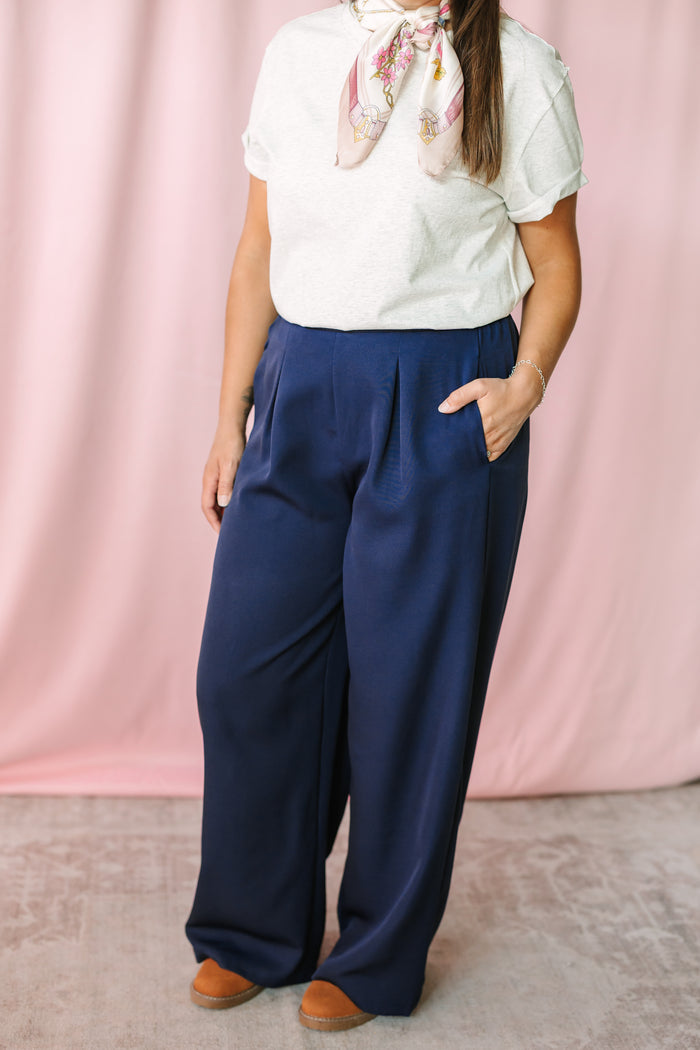 Navy wide leg dress pants worn with a gray short-sleeve top and floral silk neck scarf, full-length styling shot on pink background