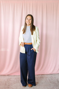 Navy wide leg dress pants paired with a cream blazer and light gray top, styled on a woman against a pink curtain backdrop