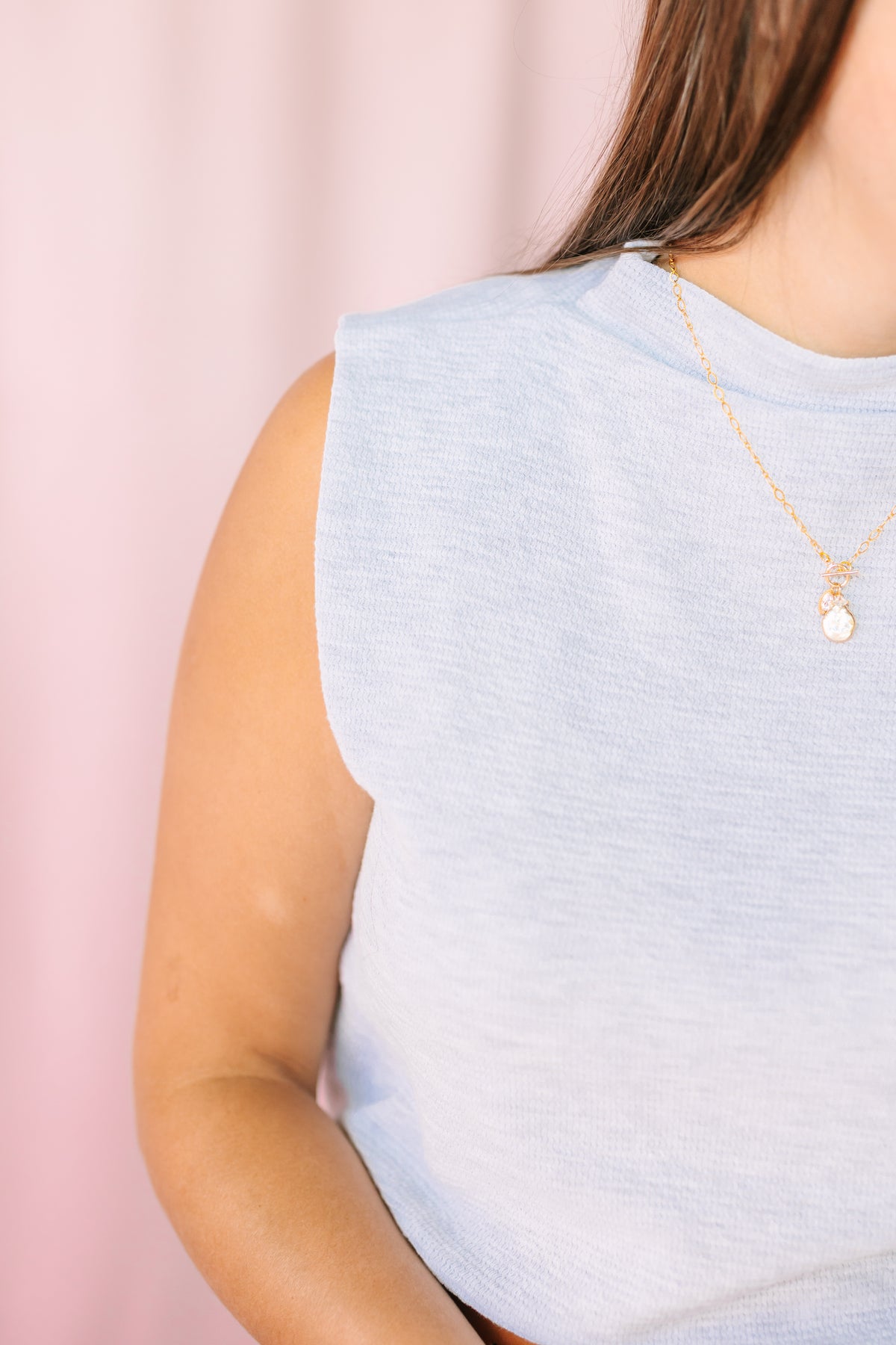 Grey mock neck sleeveless top close-up with gold pendant necklace detail, soft grey fabric texture