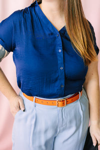 Navy blue short-sleeve button-front blouse with gathered neckline detail, paired with light blue wide-leg pants and brown leather belt
