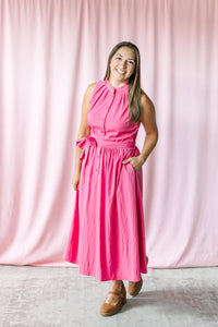 Woman wearing a berry sleeveless button-front midi dress with tie waist and pockets, styled with tan Mary Jane wedges