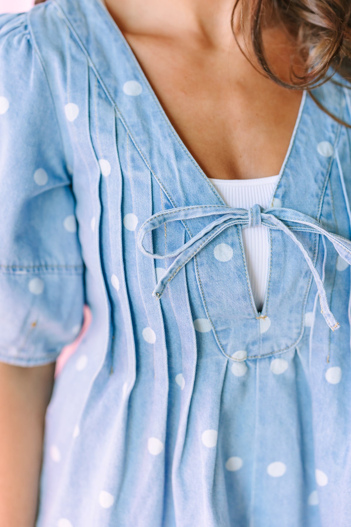 Close-up of a woman wearing a light blue denim dress with white polka dots and a tie-front detail over a white top.