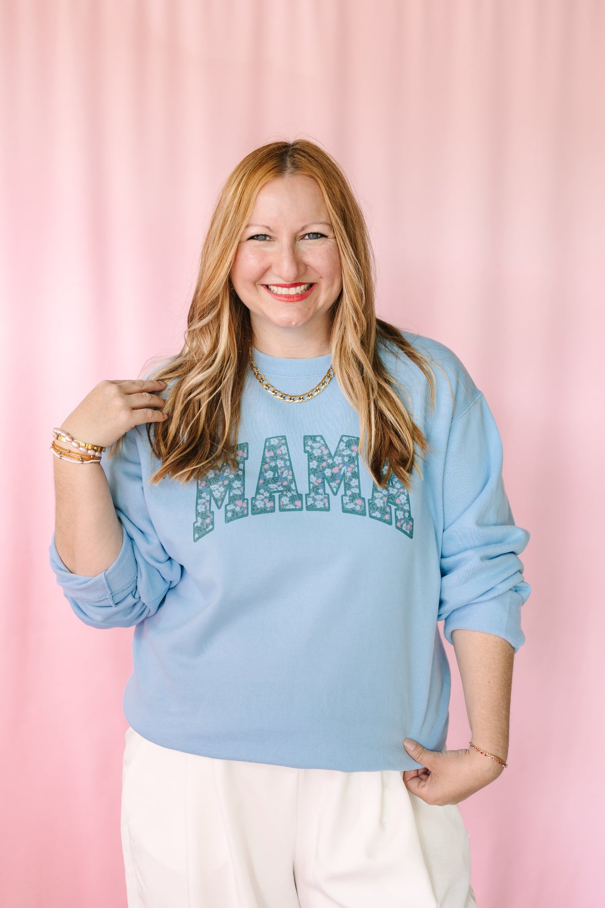 Woman wearing a light blue sweatshirt with 'MAMA' printed on it against a pink background