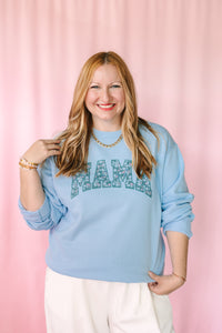 Woman wearing a light blue sweatshirt with 'MAMA' printed on it against a pink background