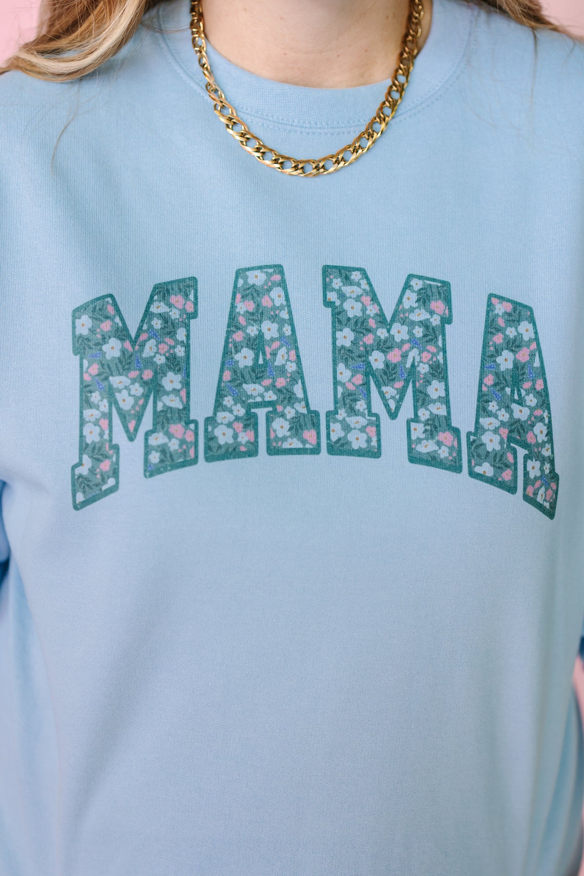 Light blue t-shirt with floral 'MAMA' text worn by a person.