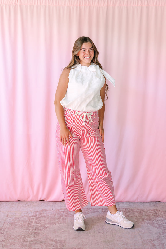 Red and white pinstripe barrel pants styled with a white ruffle top and white sneakers — full body view