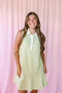 Woman smiling in a sage green gingham sleeveless polo dress with white collar and button front, pink backdrop
