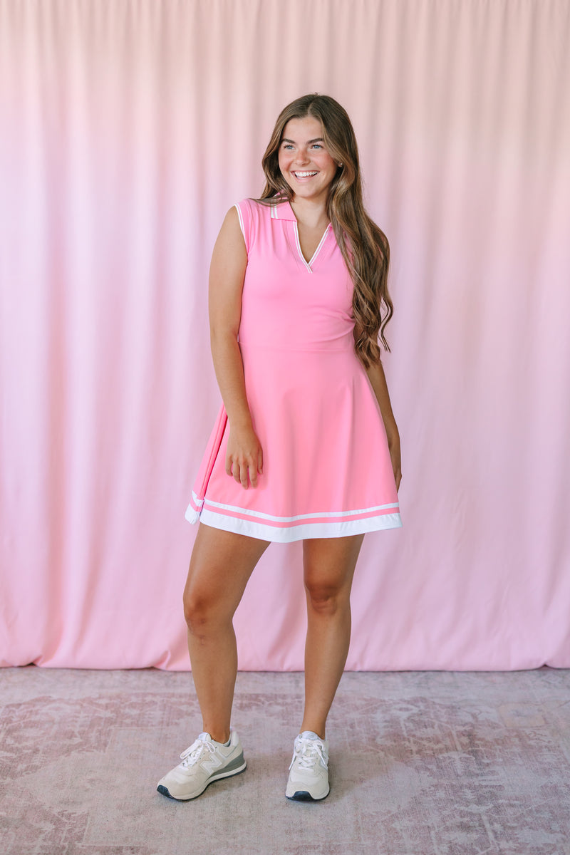 Woman wearing Pink Activewear Tennis Dress with white stripe hem detail and white sneakers, full length view
