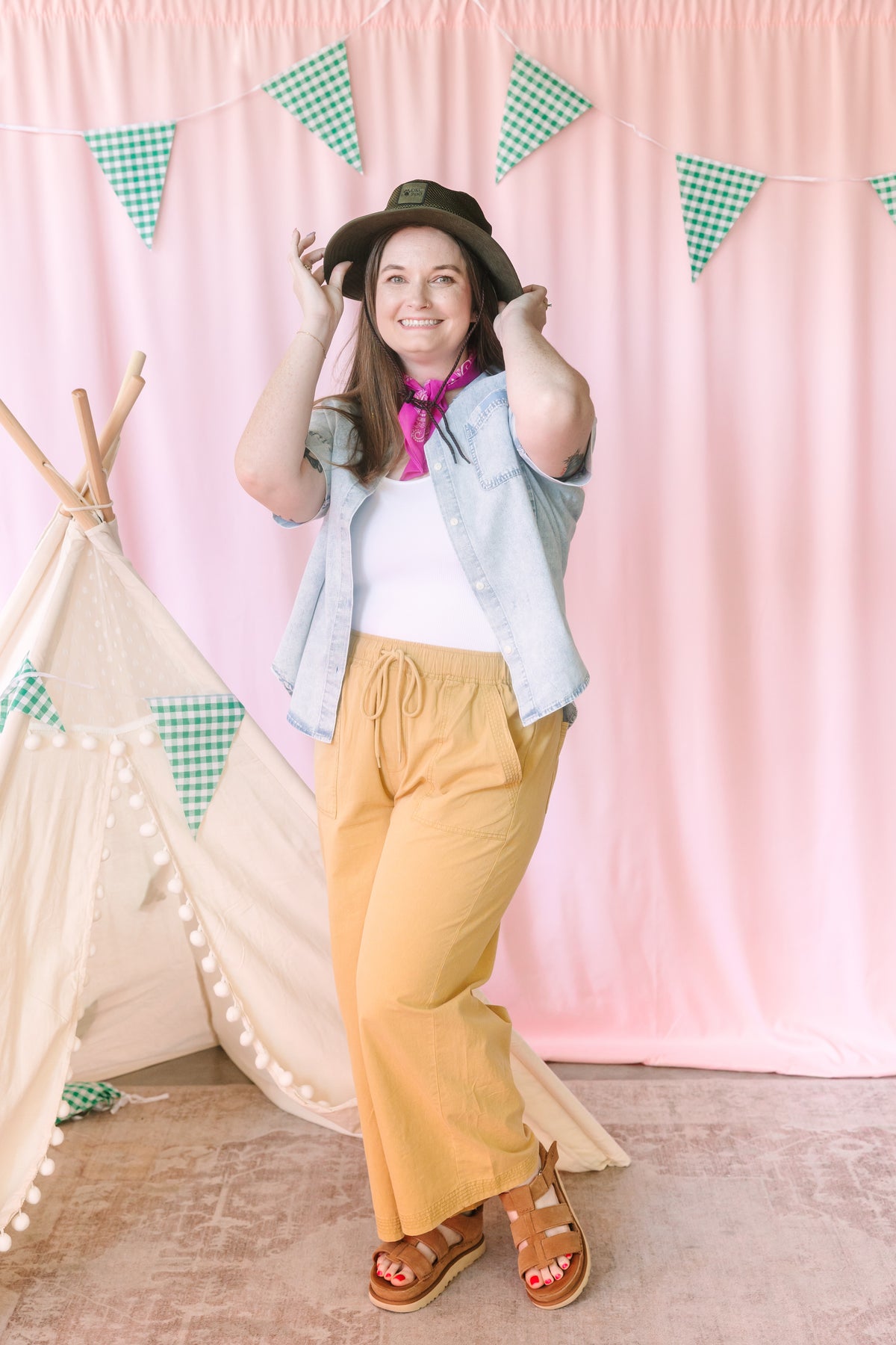 woman in golden yellow wide-leg pants styled with a white tee, denim shirt, and black hat, accessorized with a pink bandana