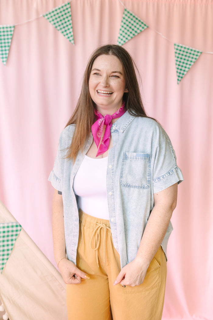 Woman in light wash denim short-sleeve button-down shirt with pink bandana and mustard wide-leg pants, front view