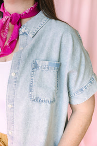 Close-up detail of light wash chambray shirt showing chest pocket and ruffle sleeve trim