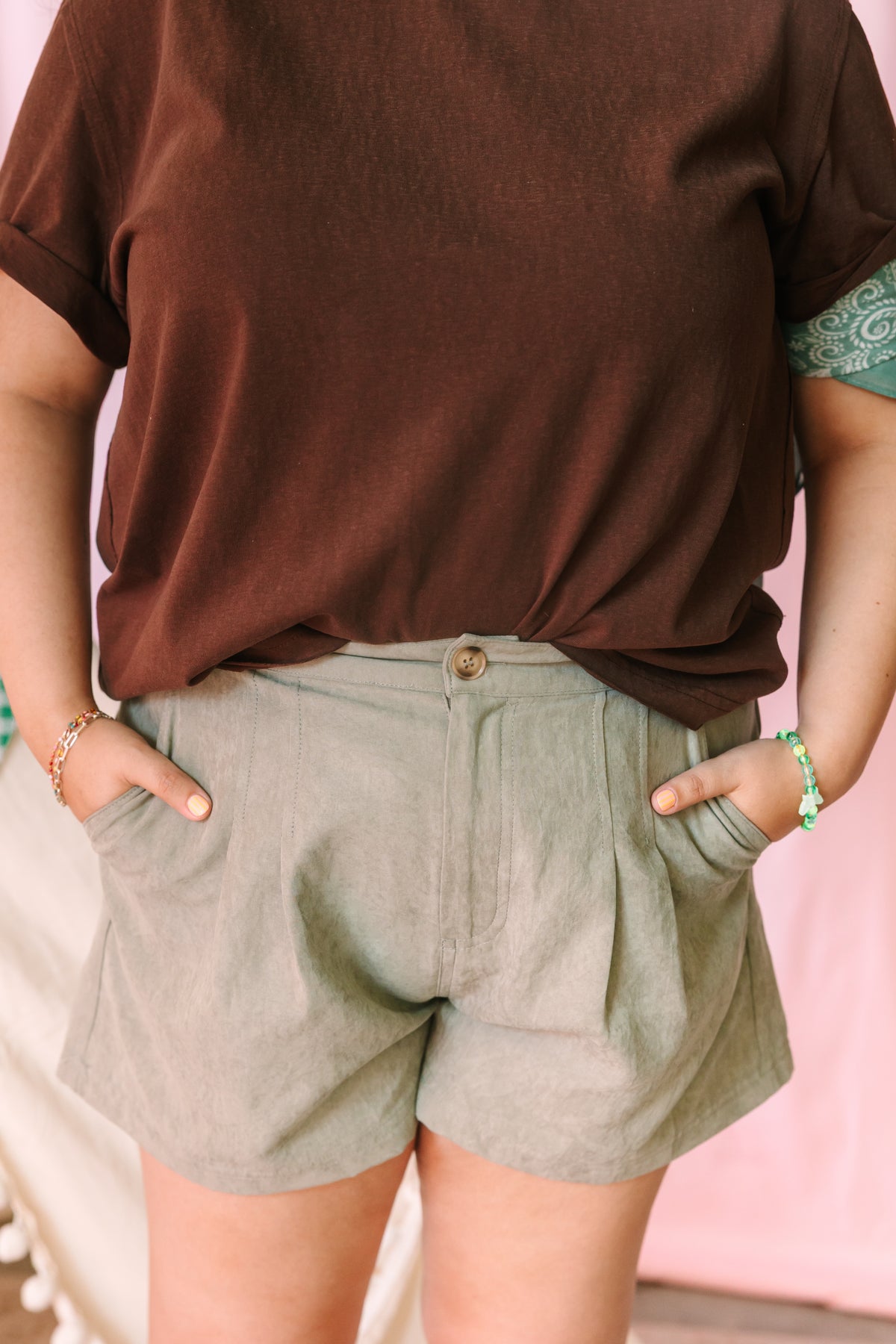 Close-up of sage green linen pleated shorts with button closure, paired with soft brown tee