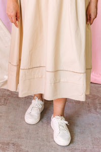 Close-up of a cream cotton midi skirt with double ladder lace trim detail near the hem, paired with white lace-up sneakers