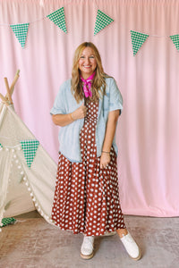Woman wearing a rust brown polka dot midi dress layered with a light wash short-sleeve denim shirt and pink bandana, styled with white platform sneakers