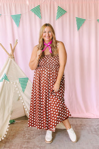 Full-length view of a rust brown and cream polka dot midi dress with smocked bodice and tiered skirt, styled with white platform sneakers and a pink bandana