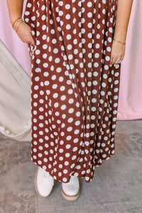 Close-up of the tiered skirt on a rust brown and white polka dot midi dress showing side pockets and flowing hem, styled with white platform sneakers