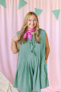 Smiling woman in sage green plus-size pleated sleeveless romper with pink paisley bandana scarf, Camp Cargo collection