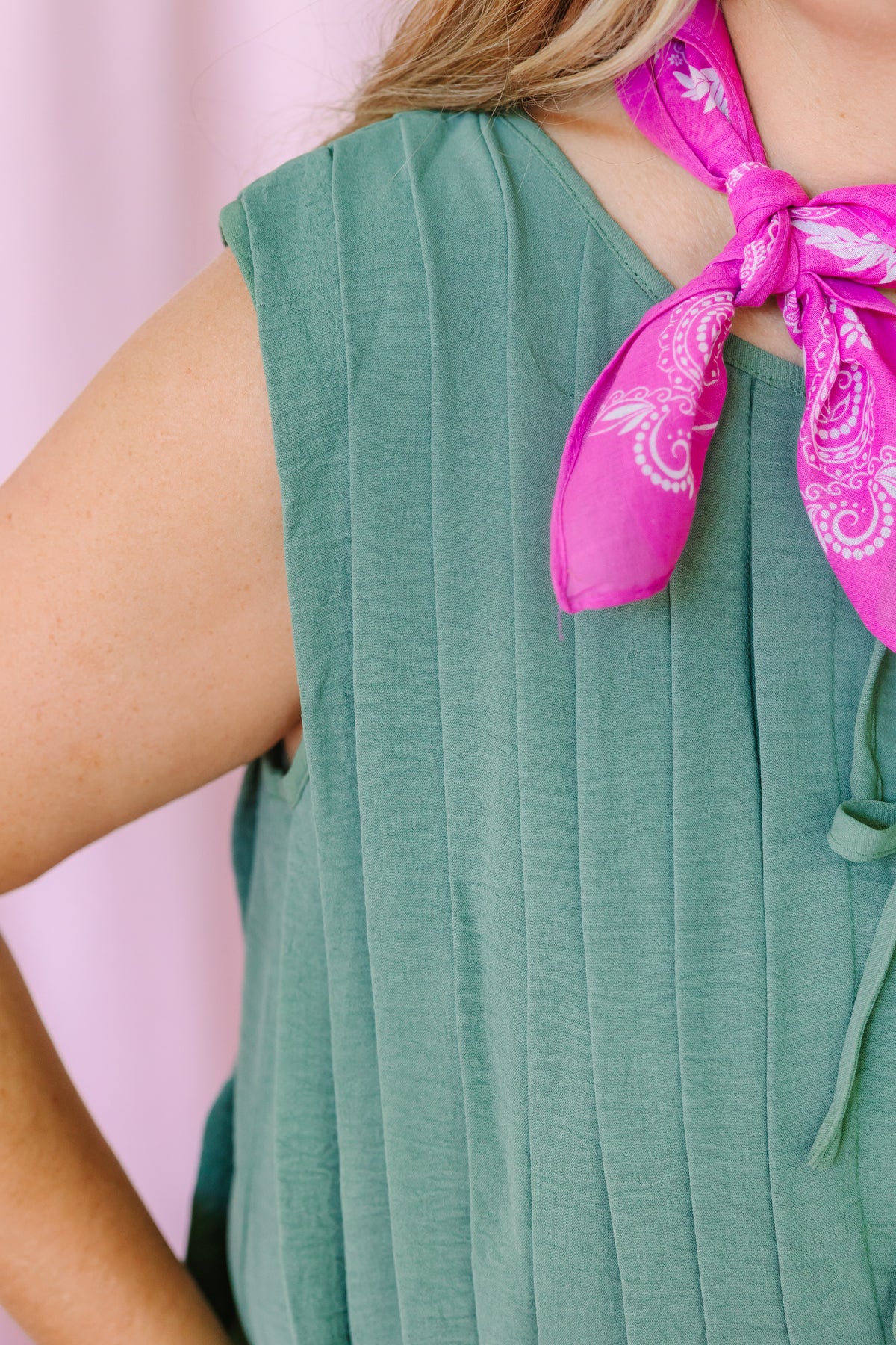 Close-up of sage green pleated romper fabric with tie front neckline and pink paisley bandana scarf detail
