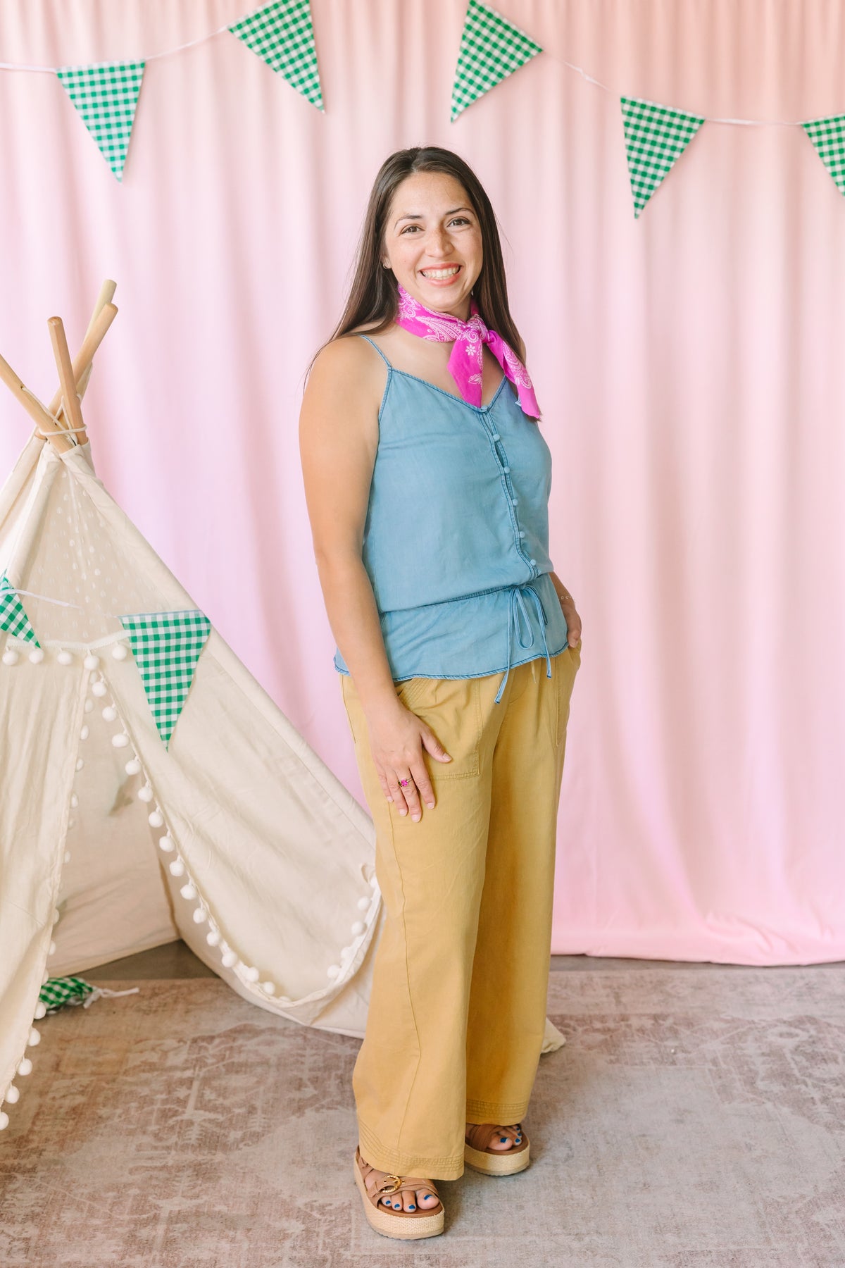 woman wearing golden yellow wide-leg pants with a blue button-front cami top and pink bandana scarf, styled with platform sandals